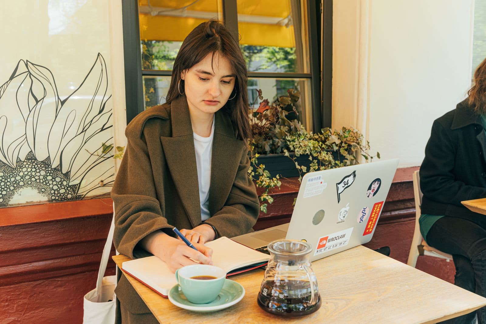 A person writing notes beside a laptop in a café